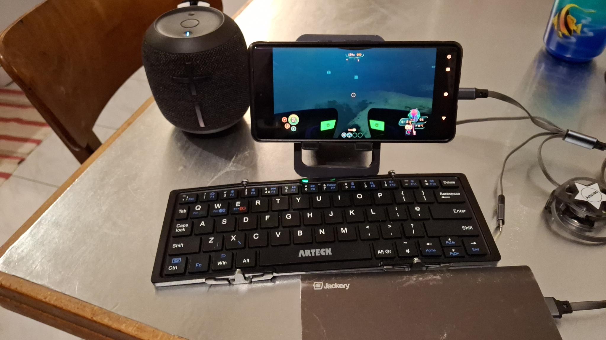 Figure 2: Watching a Twitch stream (of the game Subnautica) on Android, using a foldable phone stand, a foldable bluetooth keyboard to type to Twitch Chat, and bluetooth speakers for volume (optional). Plugged in to a portable battery for durability, by an unrollable USB cable.